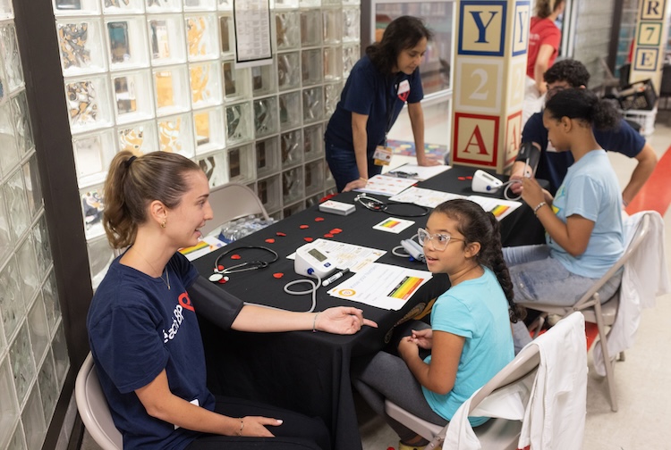 테이블이 복도에 설치되어 있습니다. 폴리 심장 센터 팀원들이 학생들과 이야기를 나누고 있습니다.