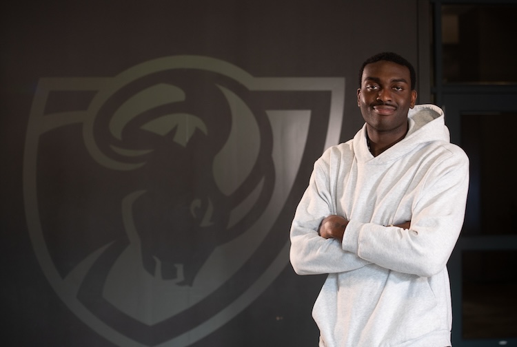 흰색 운동복을 입은 학생이 램 로고 옆에 서 있습니다.