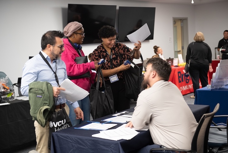 직업 박람회에서 테이블에 앉아있는 사람과 대화하는 환자와 가족 구성원.