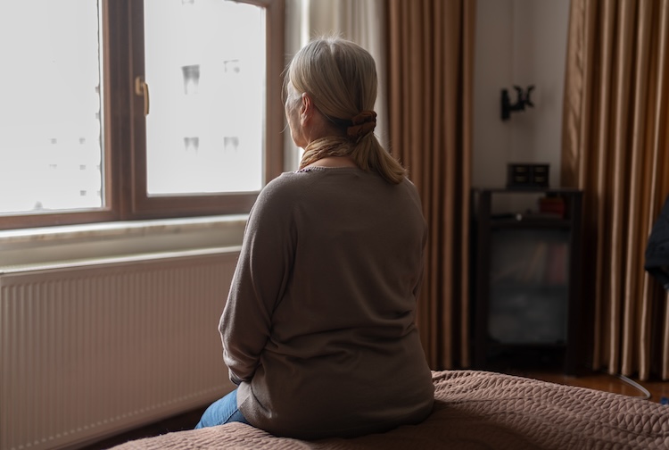 침대에 앉아 창문을 통해 바라보는 나이든 여자