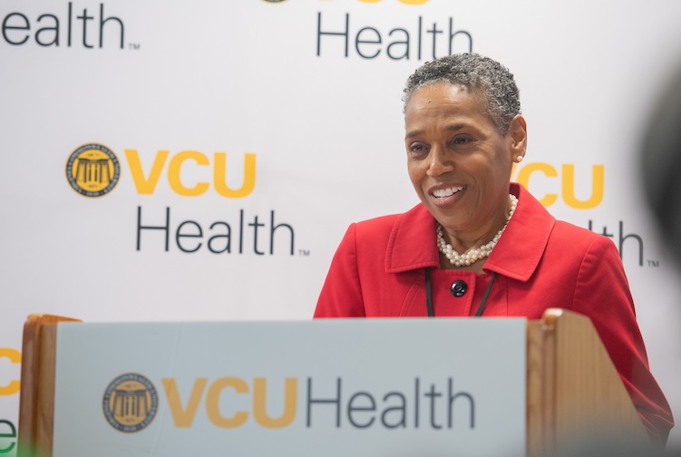 셰릴 갈랜드가 빨간색 정장 재킷을 입고 연단에 서 있습니다.