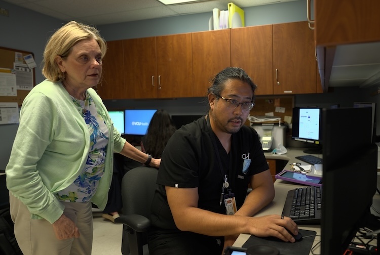 남자는 책상에 앉아 있고 여자는 어깨 너머로 환자의 스캔을 바라보고 있습니다.