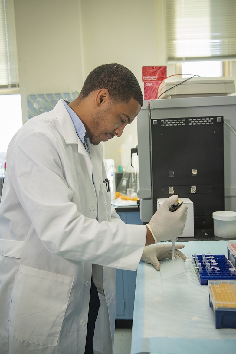 하얀 실험실 가운을 입은 남자가 피펫을 사용하여 액체를 튜브에 떨어뜨리고 있습니다.